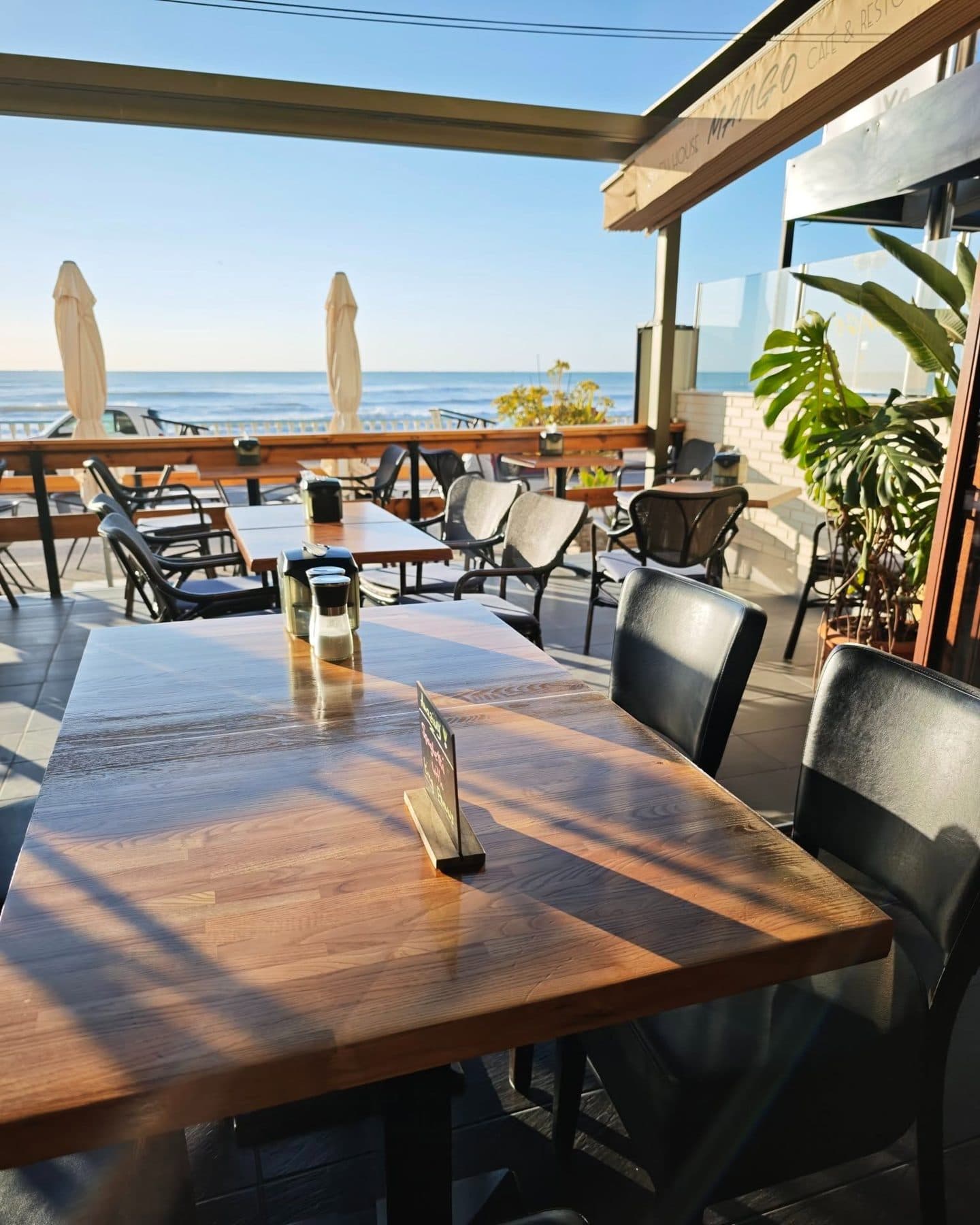 Mesas de madera de la terraza de Mango Beach House con el mar detrás, Torrevieja